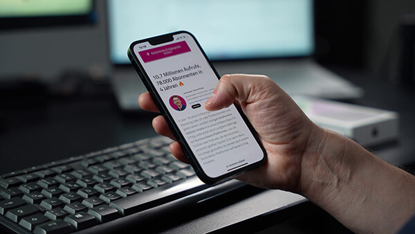 Eine Hand hält ein iPhone vor einem Schreibtisch.